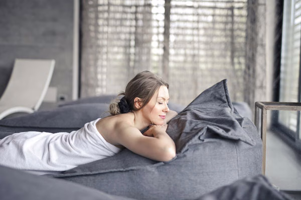 A woman in a spa relaxing on a comfortable lounge chair, surrounded by soft lighting and tranquil decor.