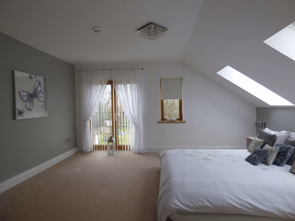 A spacious modern bedroom with large skylights and white bedding, featuring soft lighting and serene decor.